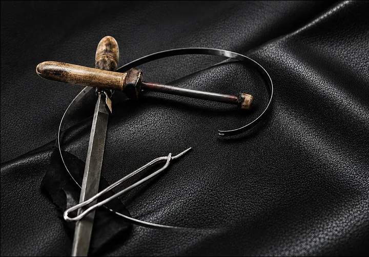 Traditional leather crafting tools awl, needle, and edge creaser on black leather